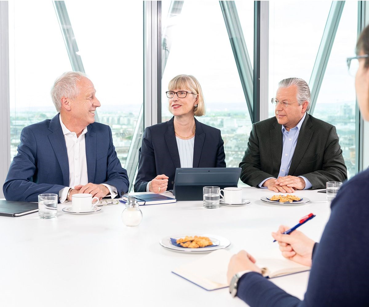 Die drei Geschäftsführenden der NHW sitzen an einem Konferenz-Tisch vor einer Fensterfront im Westhafe-ntower