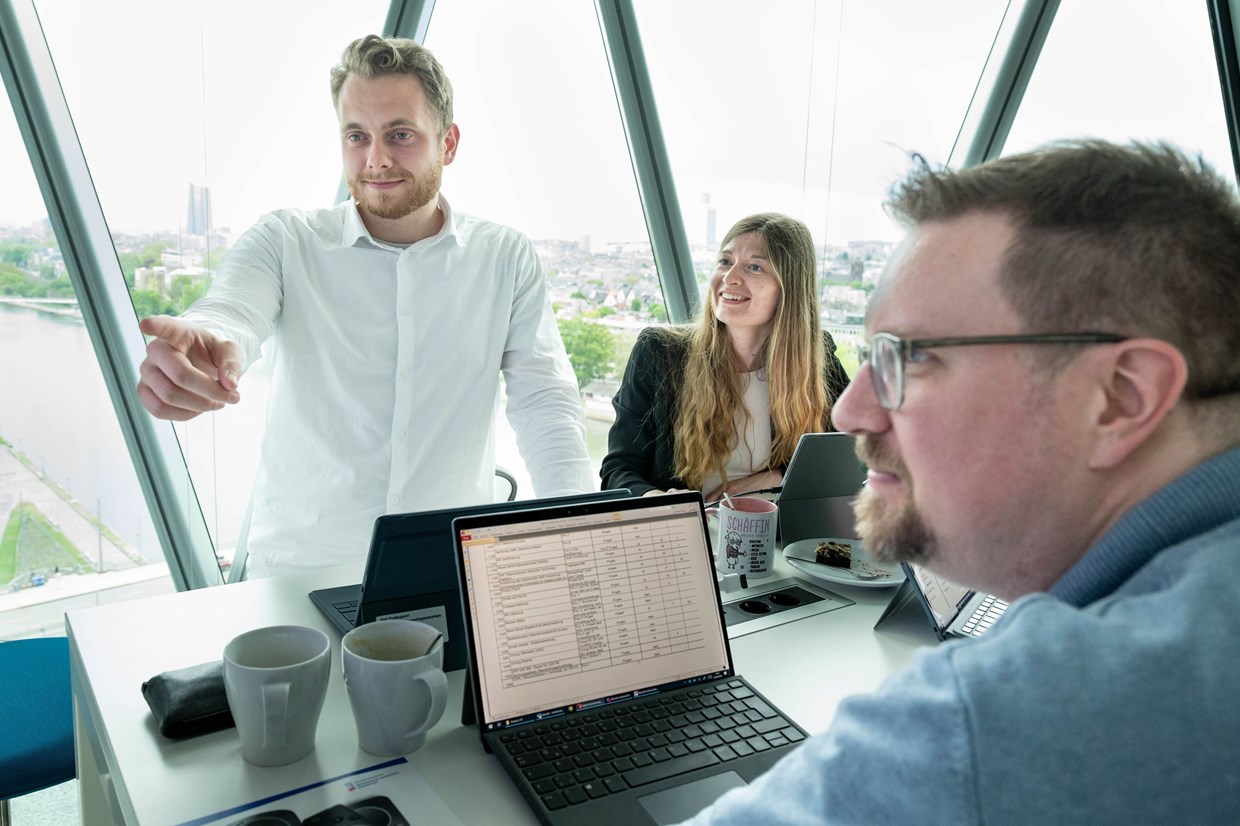 NHW Mitarbeiter sitzen an einem Schreibtisch im Westhafen-Tower mit Laptops und diskutieren lachend ein Thema