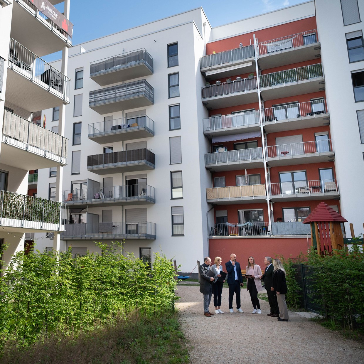 Eine 6-köpfige Gruppe von Mitarbeitern der NHW steht in einem Halbkreis auf einem Parkweg im Schönhof-Viertel in Frankfurt und tauscht sich aus.