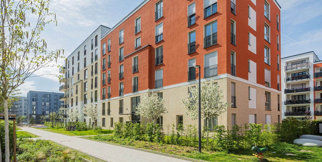 Fassadenansicht eines neu gebauten Mietshauses im Schönhof-Viertel in Frankfurt. Davor stehen blühende Kirschbäume.